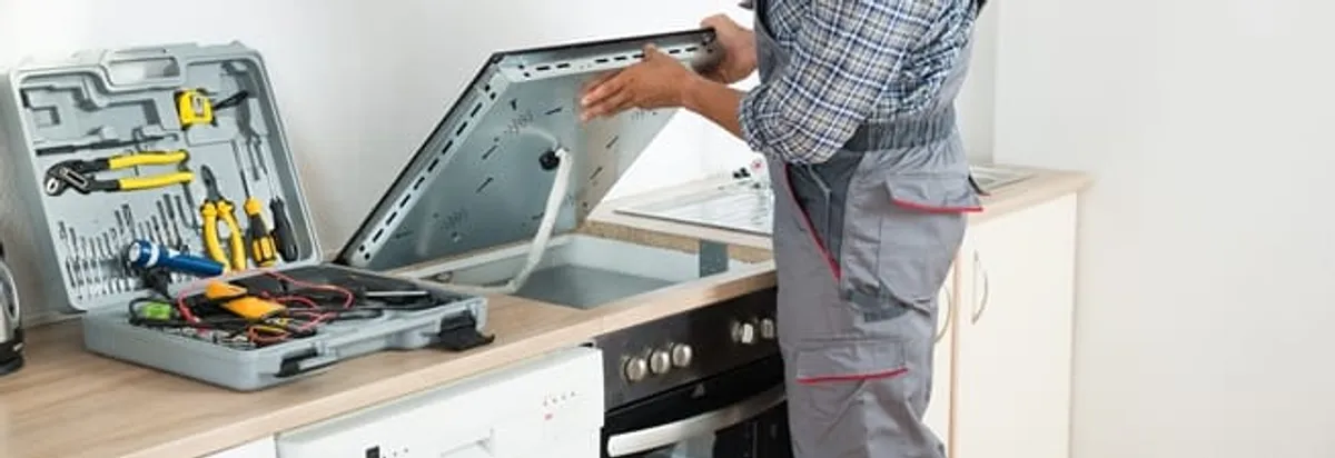 Cooktop repair technician lifting a built-in stovetop for service in Ann Arbor, MI